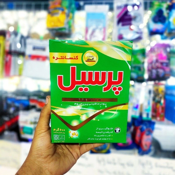 بسته پودر لباسشویی پرسیل پریمیوم 600 گرمی در دست، پسزمینه قفسه فروشگاه