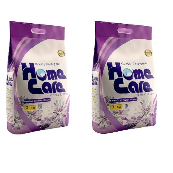 دو بسته پودر لباسشویی ۳ کیلوگرمی هوم کر با طراحی کیسه‌ ای و دستگیره سوراخ‌ دار بنفش تیره. برچسب بسته شامل نام تجاری Home Care به رنگ آبی و عبارت Quality Detergent و +Fabric Softener است. در پایین بسته‌ ها، طراحی گل‌ های سفید و بنفش به همراه شکوفه‌ های نارنجی و برگ‌ های سبز با عبارت Lavender & Orange Blossoms به چشم می‌ خورد. رنگ‌ های بنفش، آبی، نارنجی، طلایی و سبز در طراحی بسته‌ ها به کار رفته‌ اند. بسته‌ ها در کنار یکدیگر و در مرکز کادر قرار دارند.