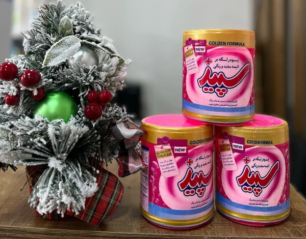 سه بسته پودر لکه‌ بر سپید با فرمولاسیون طلایی (Golden Formula) در کنار تزئینات کریسمسی شامل درخت کاج، توت قرمز و گوی سبز، مناسب برای شستشوی لباس‌ های سفید و رنگی با کیفیت بالا
