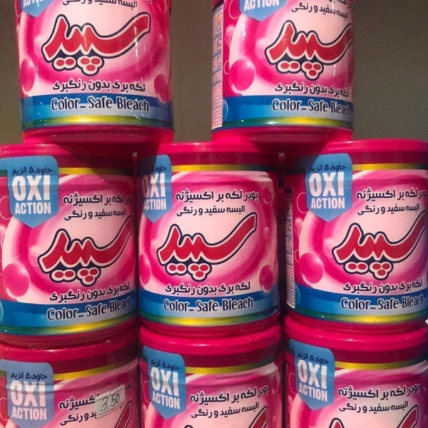 چند قوطی پودر لکه بر لباس سپید مدل oxi active با درب صورتی و برچسب OXI ACTION در قفسه فروشگاه